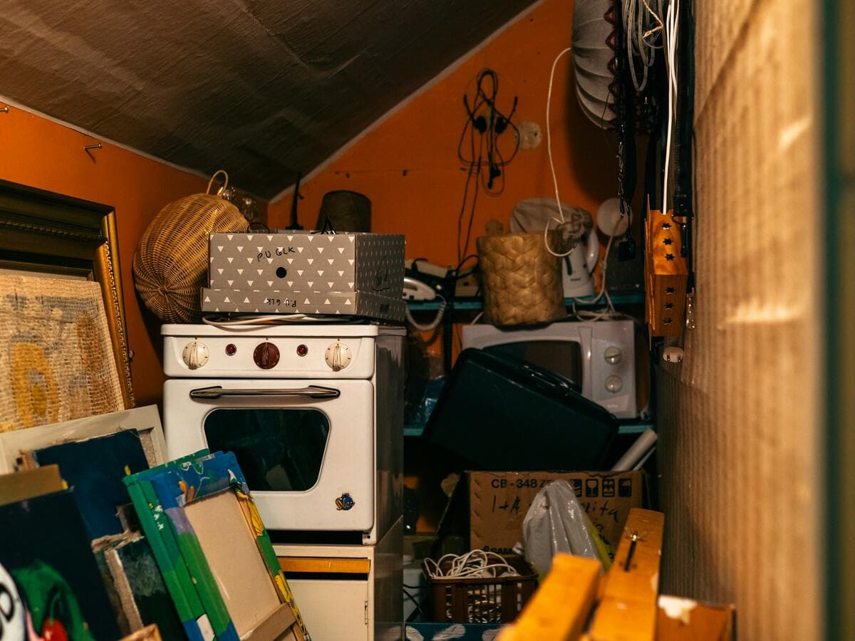 Pièce sous les combles encombrée d’une vieille cuisinière, de cartons, de cadres et d’objets entassés